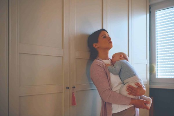Sad mom holding baby in her arms leaning against wall