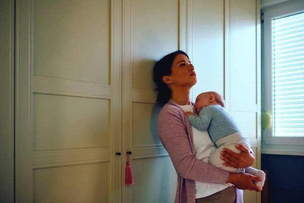 Distraught mother thinking of something while her baby is napping in her arms. Copy space.